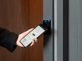 A hand holding a smartphone touching it to an access control reader for entry into a building